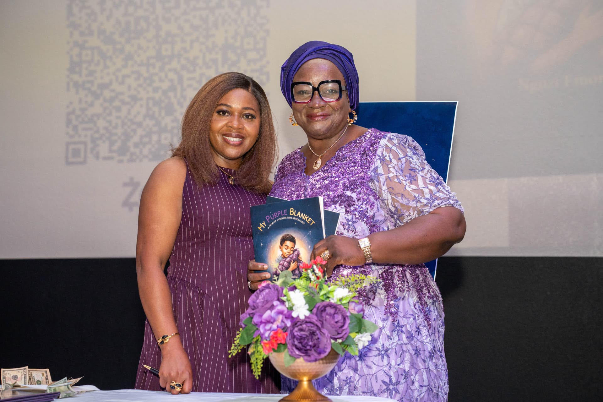Ngozi with a guest holding up two copies of My Purple Blanket at the launch table